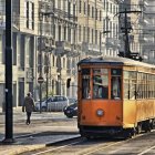 Vintage orange tram on sunlit street with pedestrians