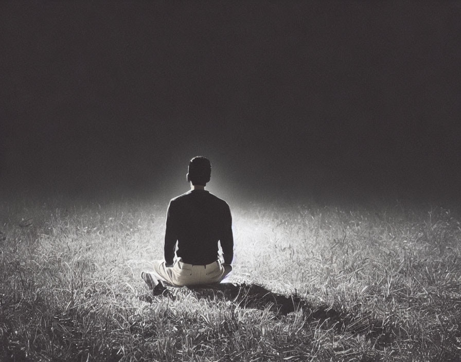 Meditating person casting shadow in dimly lit field