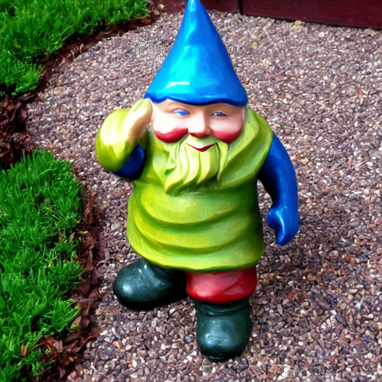 Colorful Garden Gnome Statue with Blue Hat and Red Pants on Gravel Near Grass Edge