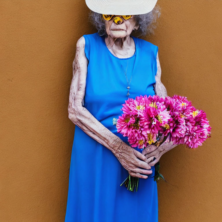 Elderly person in blue dress holding pink flowers against orange wall