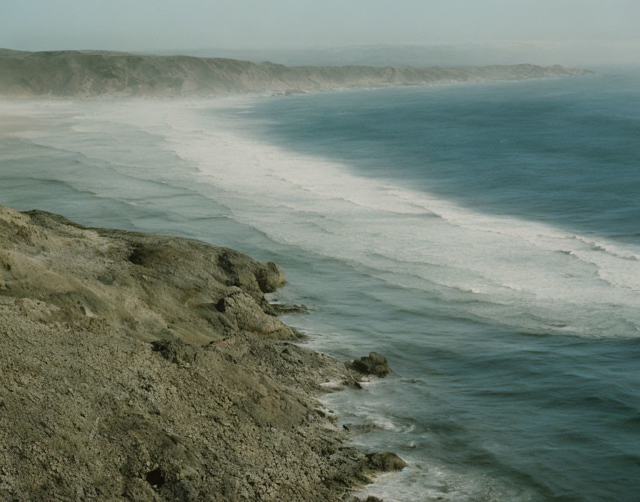 Cliffside coastline with beach, waves, and distant headland