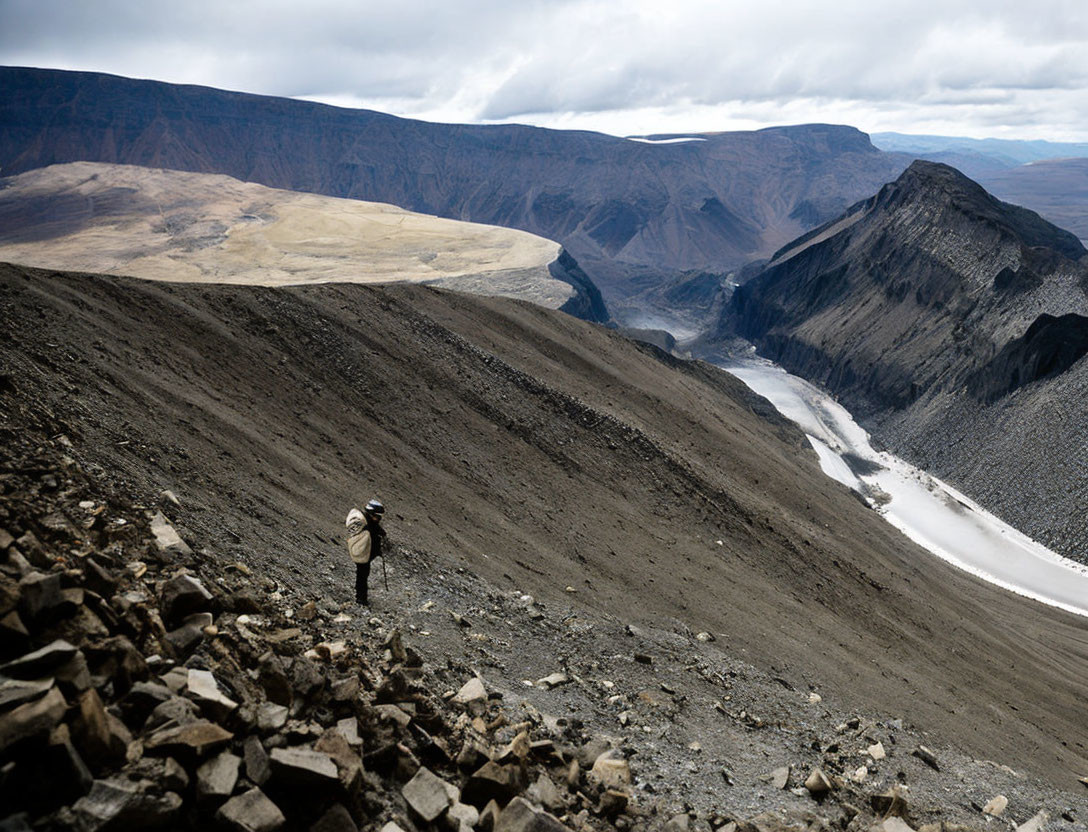 Person overlooking valley, river, mountains on rocky slope under cloudy sky