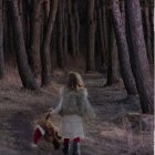 Person in white dress and hat walking on forest path surrounded by tall trees