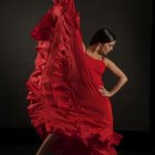 Woman in flowing red dress striking dynamic pose against dark background