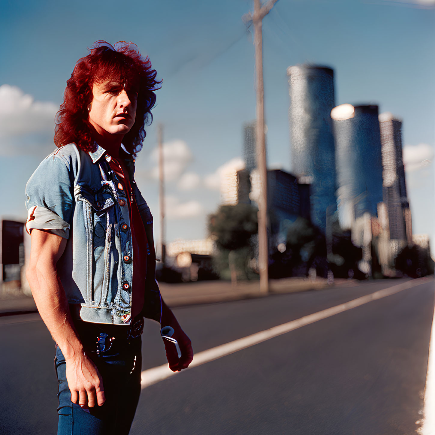 Red mullet hairstyle person in denim vest on city road with skyscrapers.