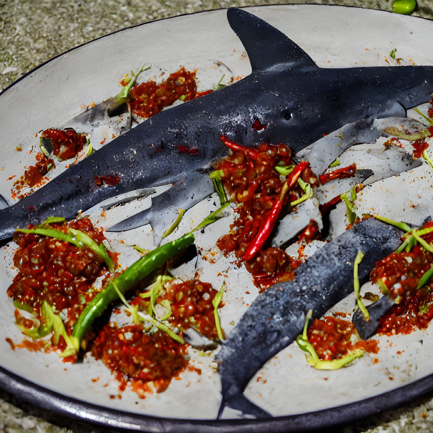 Shark-shaped dish in spicy red sauce with chilies and sprouts