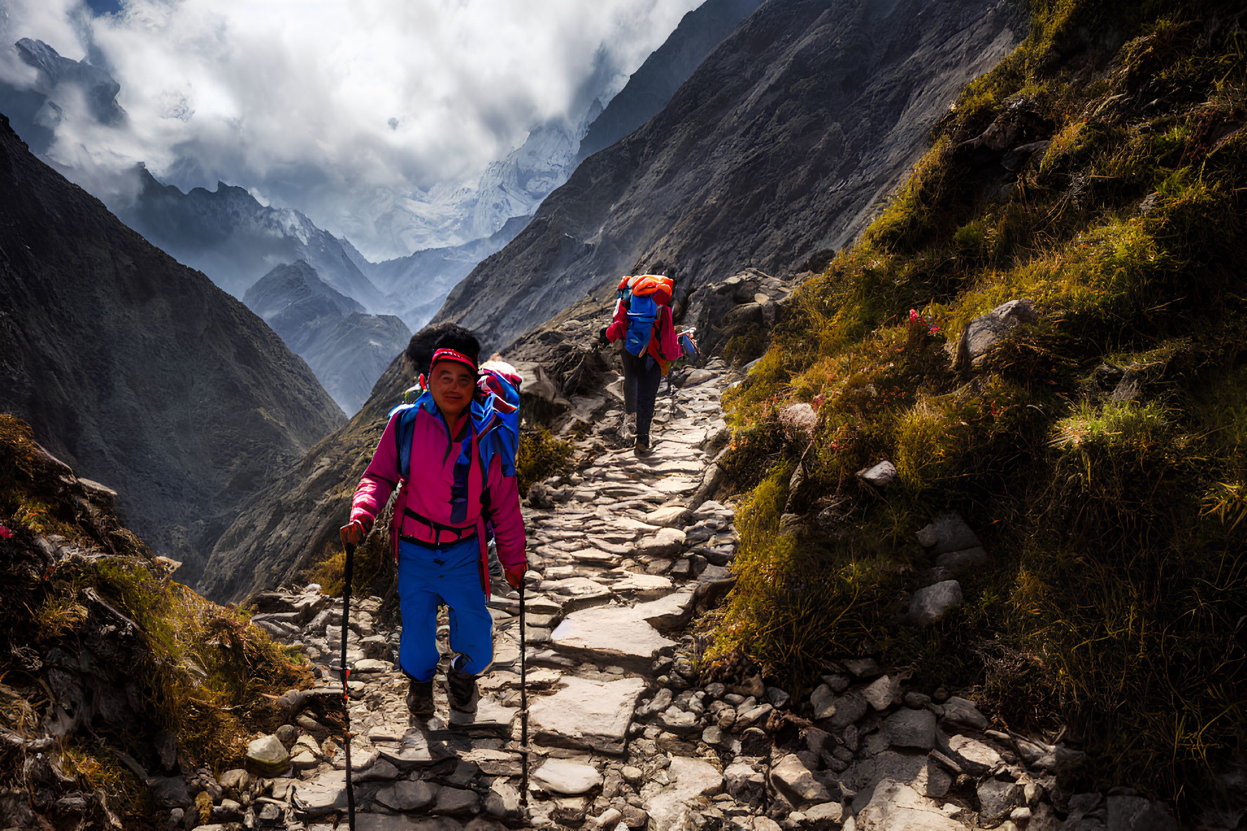 Hikers trekking on rocky mountain path with lush greenery and misty peaks