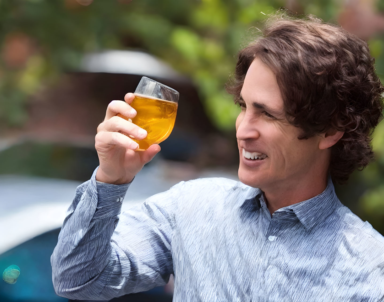 Man in Blue Shirt Smiling with Glass of Amber Liquid in Garden