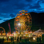 Colorful night fair with lit Ferris wheel and lively crowd.