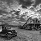 Vintage pickup truck near old wooden house under dramatic sky