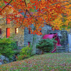 Stone cottage by autumn waterwheel in forest with stream.