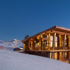 Snow-covered wooden chalet balcony in dusk with snowy mountains.