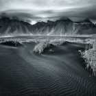 Rippled sand dunes with grass under cloudy sky and mountains