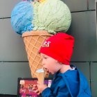 Blond child in blue jacket with giant melting ice cream cone