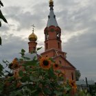 Gothic church spires amid lush greenery and red flowers against dramatic sky