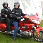 Two women in black leather outfits with red hair by red motorcycle in mountain setting