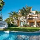 Tropical villa with red accents, palm trees, flowers, and blue pool.