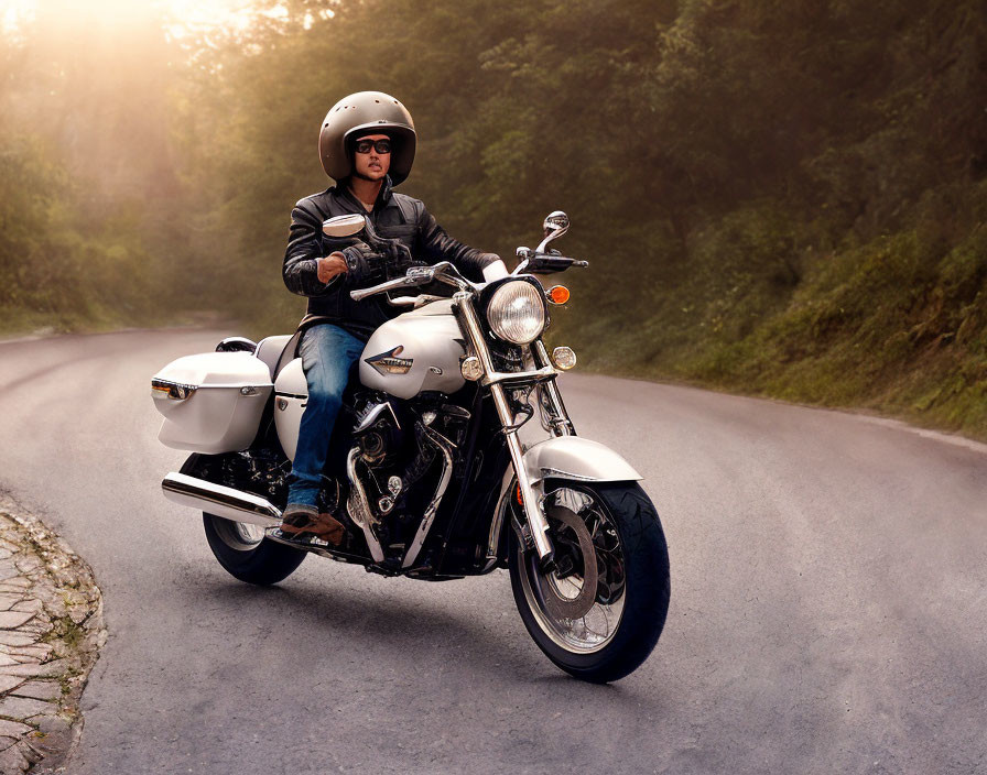 Person riding classic motorcycle with white saddlebags on curved road in greenery