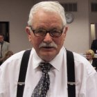 Elderly man in glasses, suspenders, and colorful tie in urban setting.