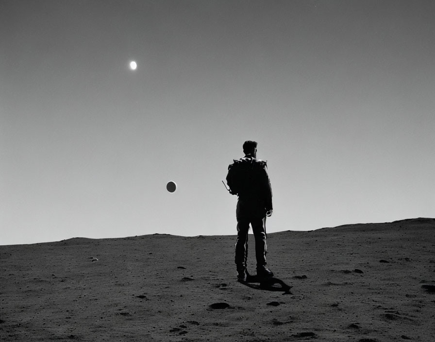 Astronaut on barren rocky landscape gazes at distant sun and celestial body