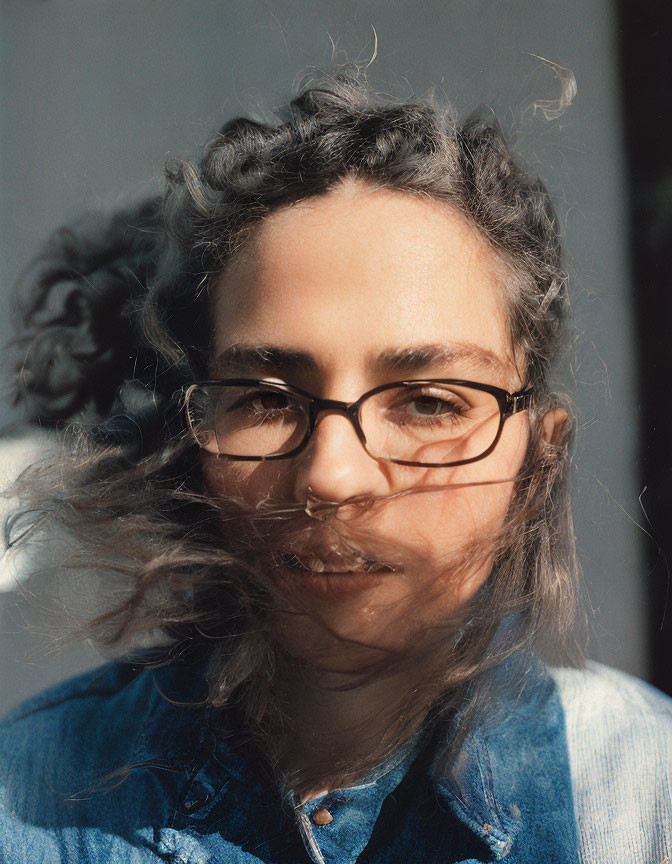 Person with Curly Hair in Denim Jacket and Glasses under Sunlight Shadows