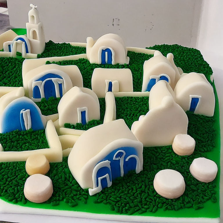 Quaint village cake with white buildings and blue roofs on green base