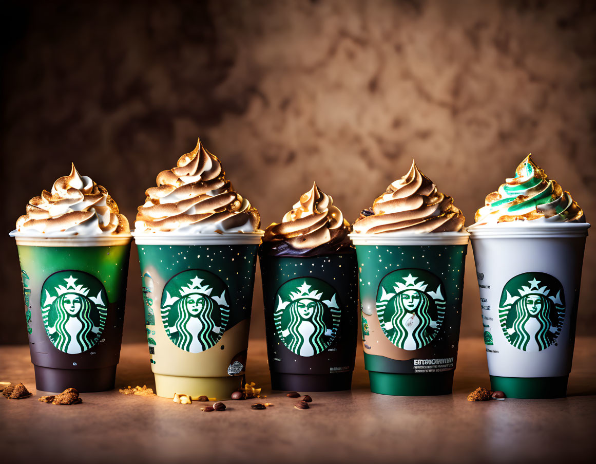 Five Starbucks seasonal drinks with whipped cream and toppings on a brown textured table