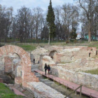 Ancient Roman bath complex with stone arches, pillars, greenery, and warm pools