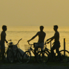 Men with bicycles observe stormy beach scene with towering waves