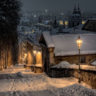 Snow-covered cabin beside glowing street lamp in serene snowfall night.