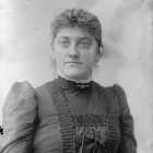 Young woman in vintage black and white photo with floral dress and hat.