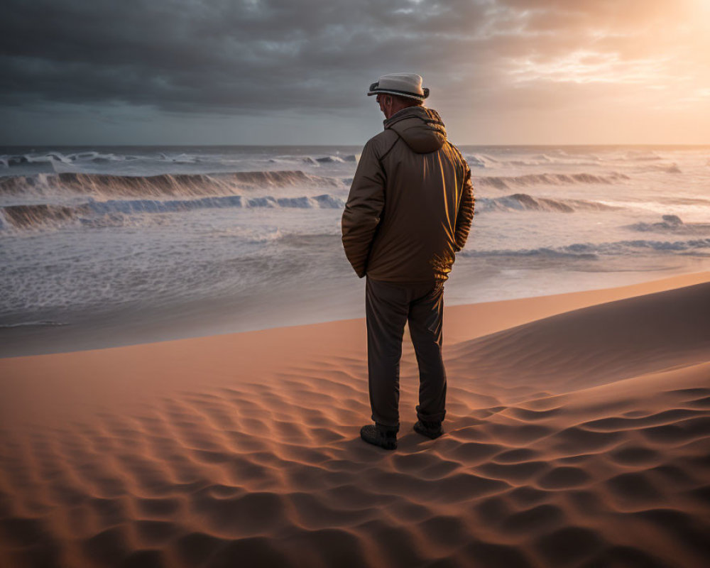 Person in hat and jacket on sandy beach at sunset watching waves crash under dramatic sky