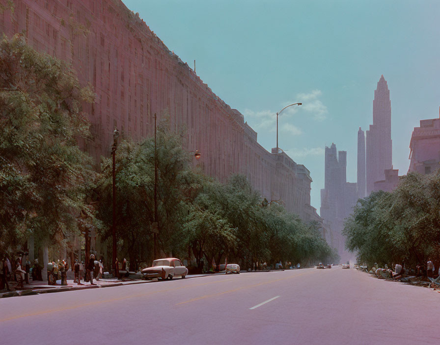 Vintage city street with trees, classic cars, tall buildings under clear sky