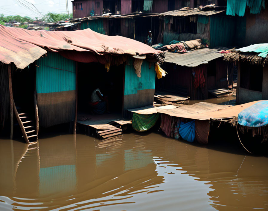 Flooded ramshackle houses with corrugated roofs and belongings on elevated platforms.