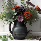 Antique black jug with orange poppies bouquet on rustic white wooden backdrop