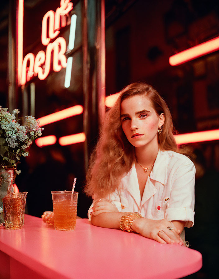 Woman sitting at pink table in neon-lit retro setting with drinks