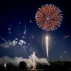 Person sitting under night sky watching golden and red fireworks