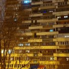 Urban apartment building with starry night sky, lit windows, trees, and streetlights.