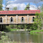 Wooden covered bridge over serene stream in lush greenery and blooming flowers