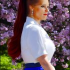 Red-haired woman in ponytail with white blouse and blue skirt among pink cherry blossoms