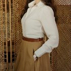 Vintage Woman in White Blouse and Tan Skirt Stands by Gold Ornate Screen