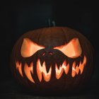 Carved pumpkin with spider silhouette on leaf for Halloween.