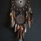 Two circular dreamcatcher webs with feathers and beads on dark background