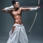 Muscular man in white dhoti, drawing bow and arrow with intense expression