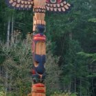 Colorful Totem Pole with Ornate Bird in Tranquil Forest Setting