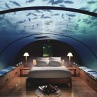 Luxurious underwater bedroom with large bed, seating, glass dome ceiling, swimming fish, mood lighting