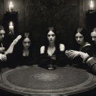 Pallid individuals in dark attire at circular table with candles