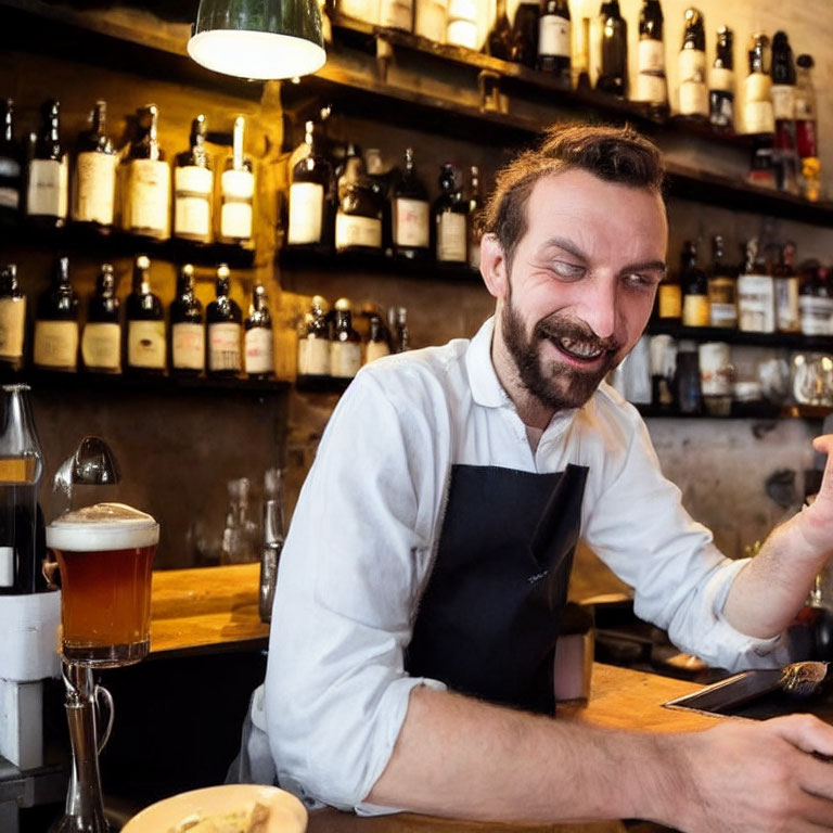 Smiling bartender with beard in apron at bar with bottles and beer