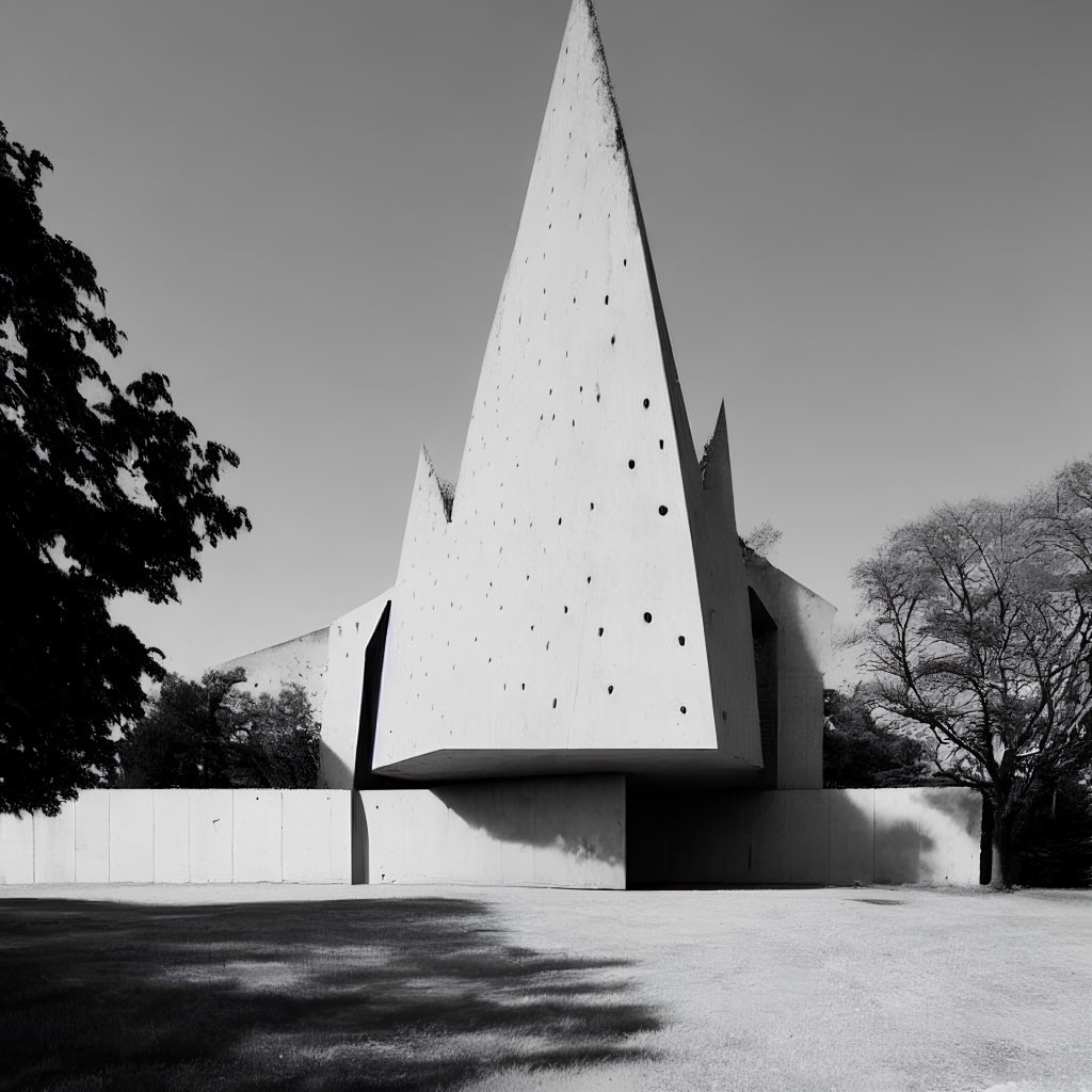 Monochrome photo of sharp triangular modern architecture building with dotted facade surrounded by trees