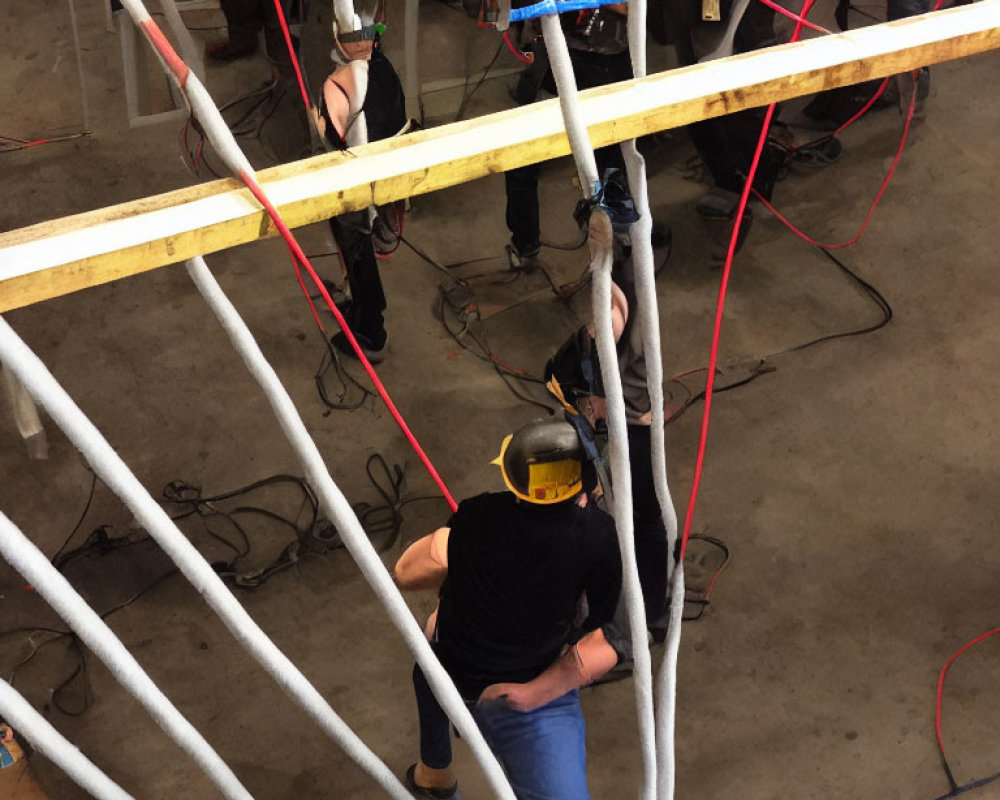 Person in Yellow Hard Hat in Workshop Setting with Others Working